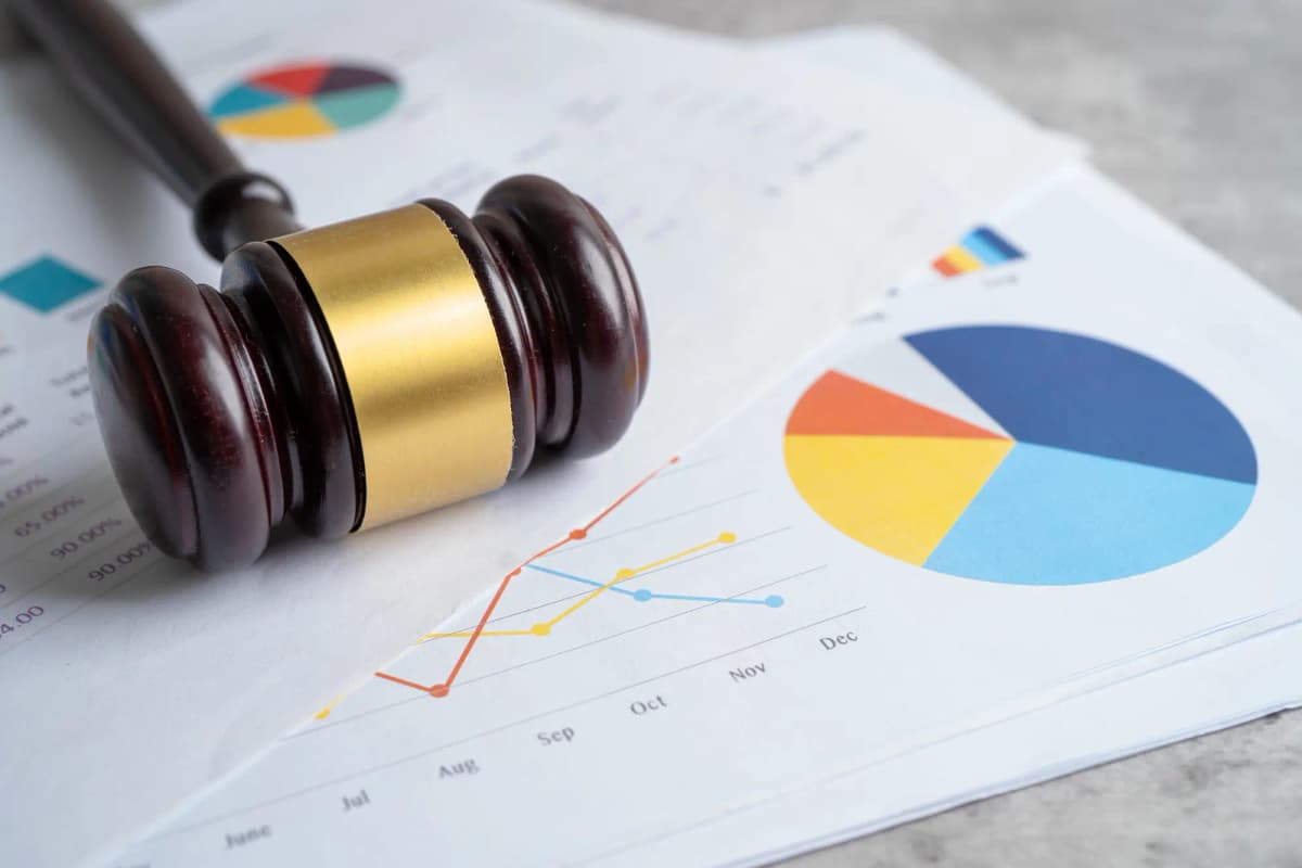 Wooden judge's gavel resting on printed charts and graphs, symbolizing legal action, compliance, audits, or regulatory enforcement.