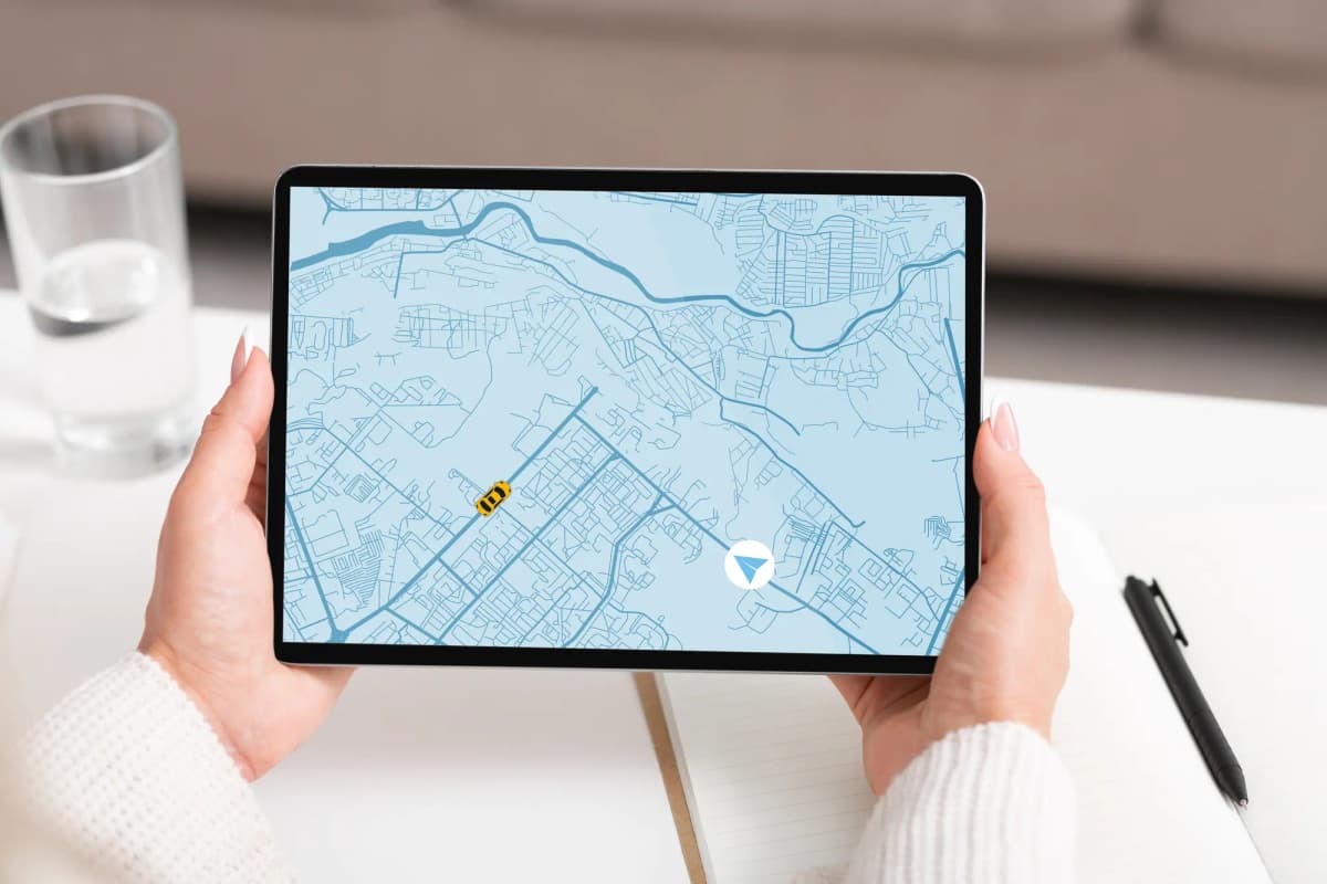 Person holding a tablet displaying a digital map with roads, locations, and navigation markers.