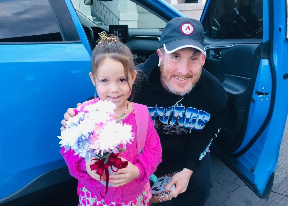 Tanner, a blind father, gives his daughter a bouquet of flowers. She smiles while holding them, capturing their close bond and warmth.