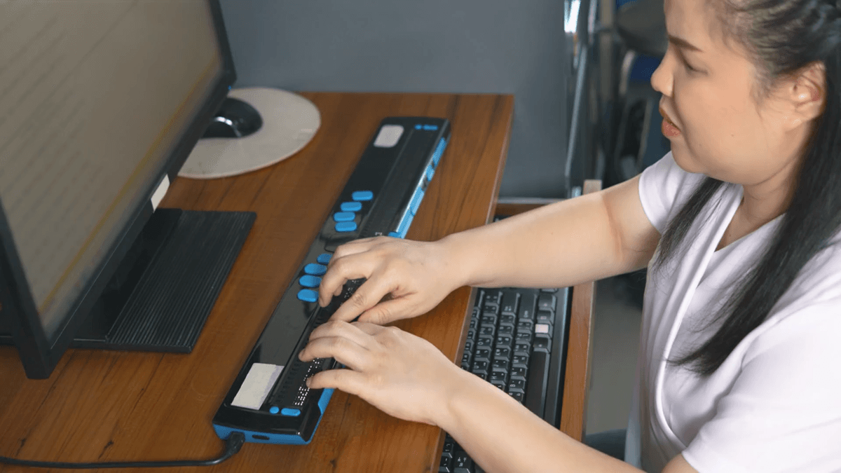 A blind woman working with her computer and using a braille display.