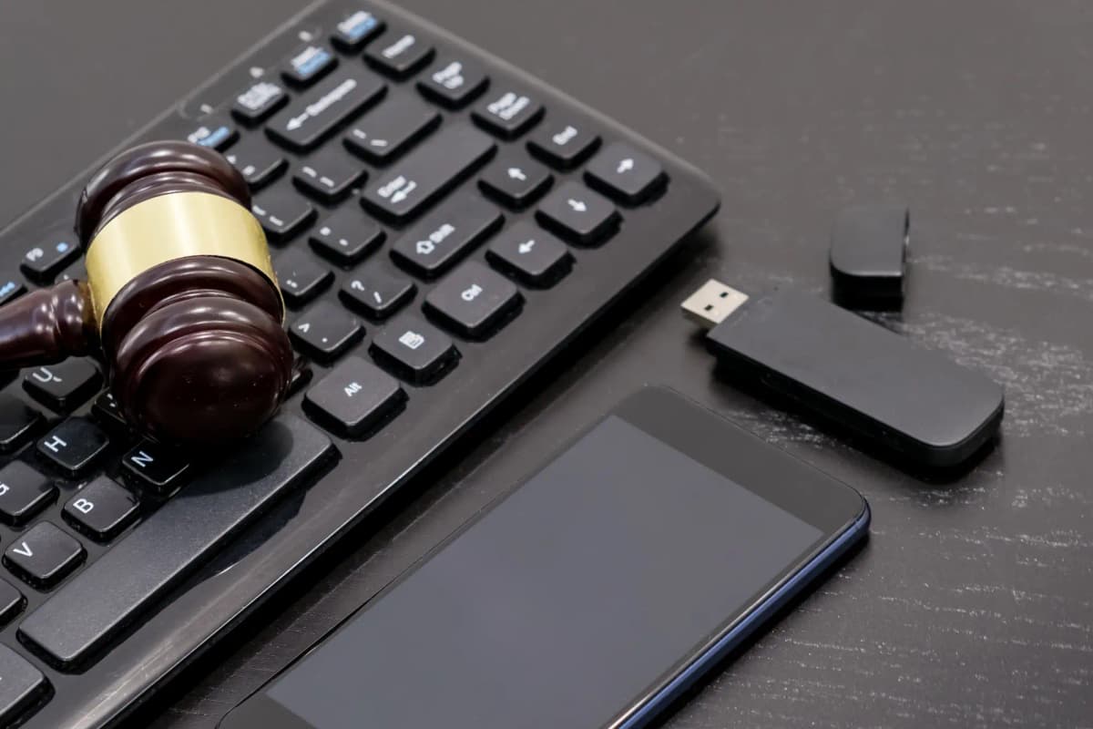 Wooden gavel on black keyboard with phone and USB on a dark desk, modern legal workspace