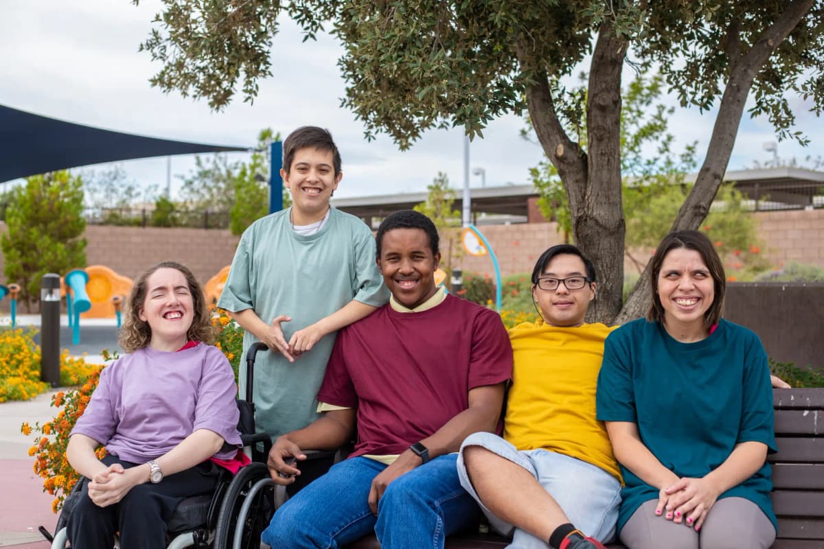Group of people with disabilities sitting together on a park bench outdoors, smiling and socializing