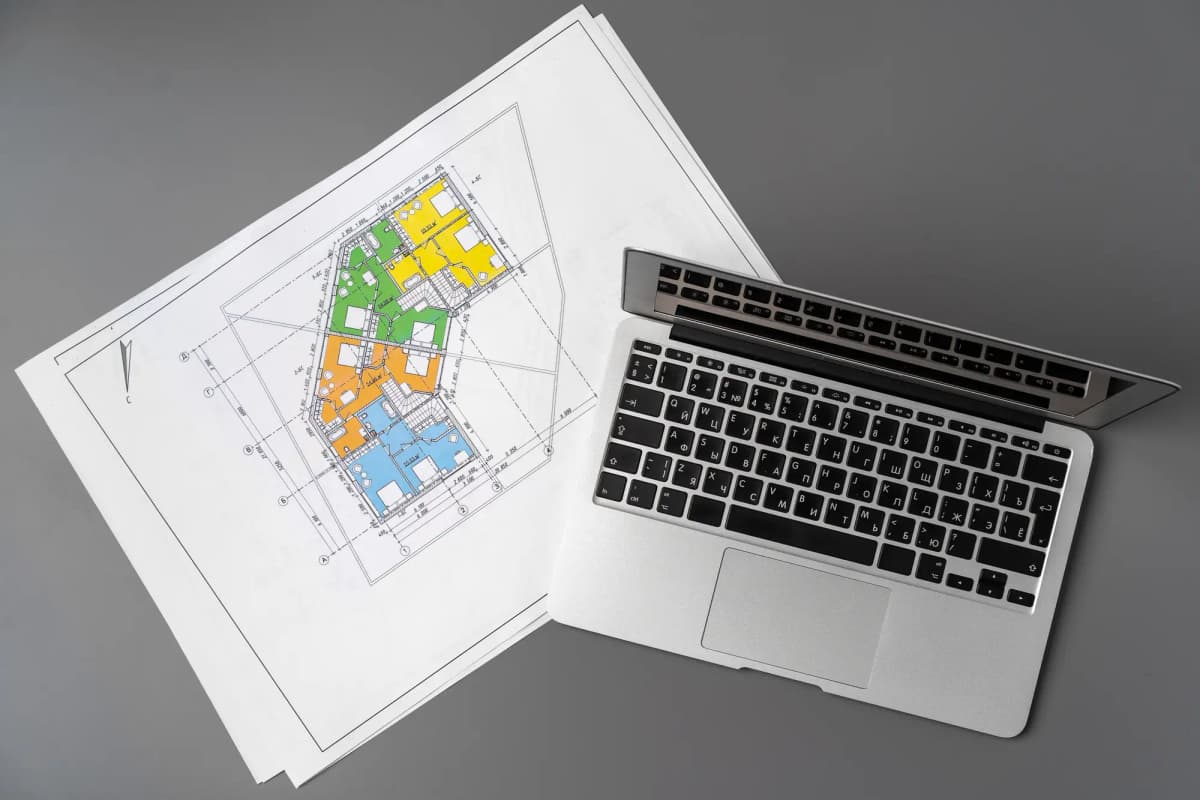 Laptop beside printed floor plans on a gray desk, clean workspace with technical drawings