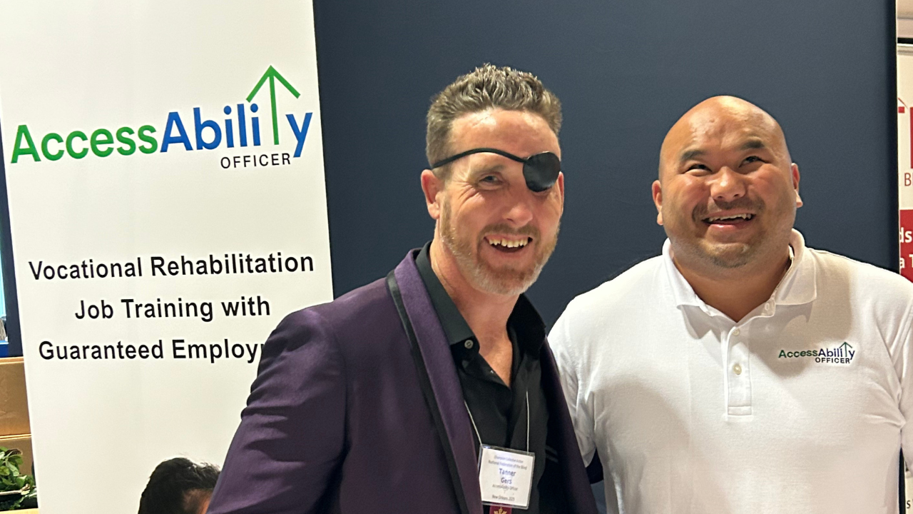 Tanner Gers and Bee Yang from AccessAbility Officer smiling together at the 2025 NFB Conference in front of a banner promoting vocational rehabilitation job training and guaranteed employment.