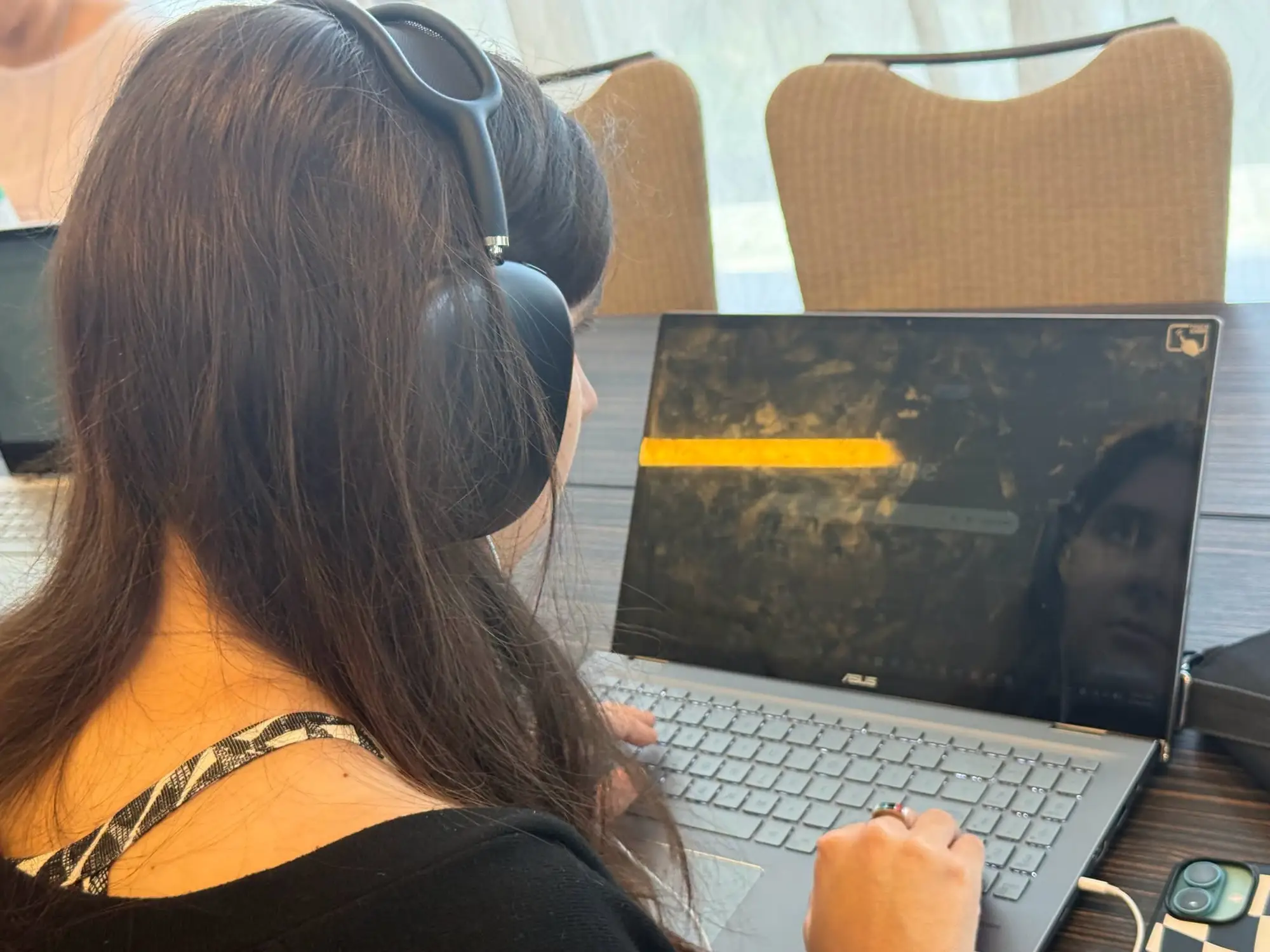 A person with long dark hair, wearing black over-ear headphones and seen from behind, types on an ASUS laptop during the testathon.