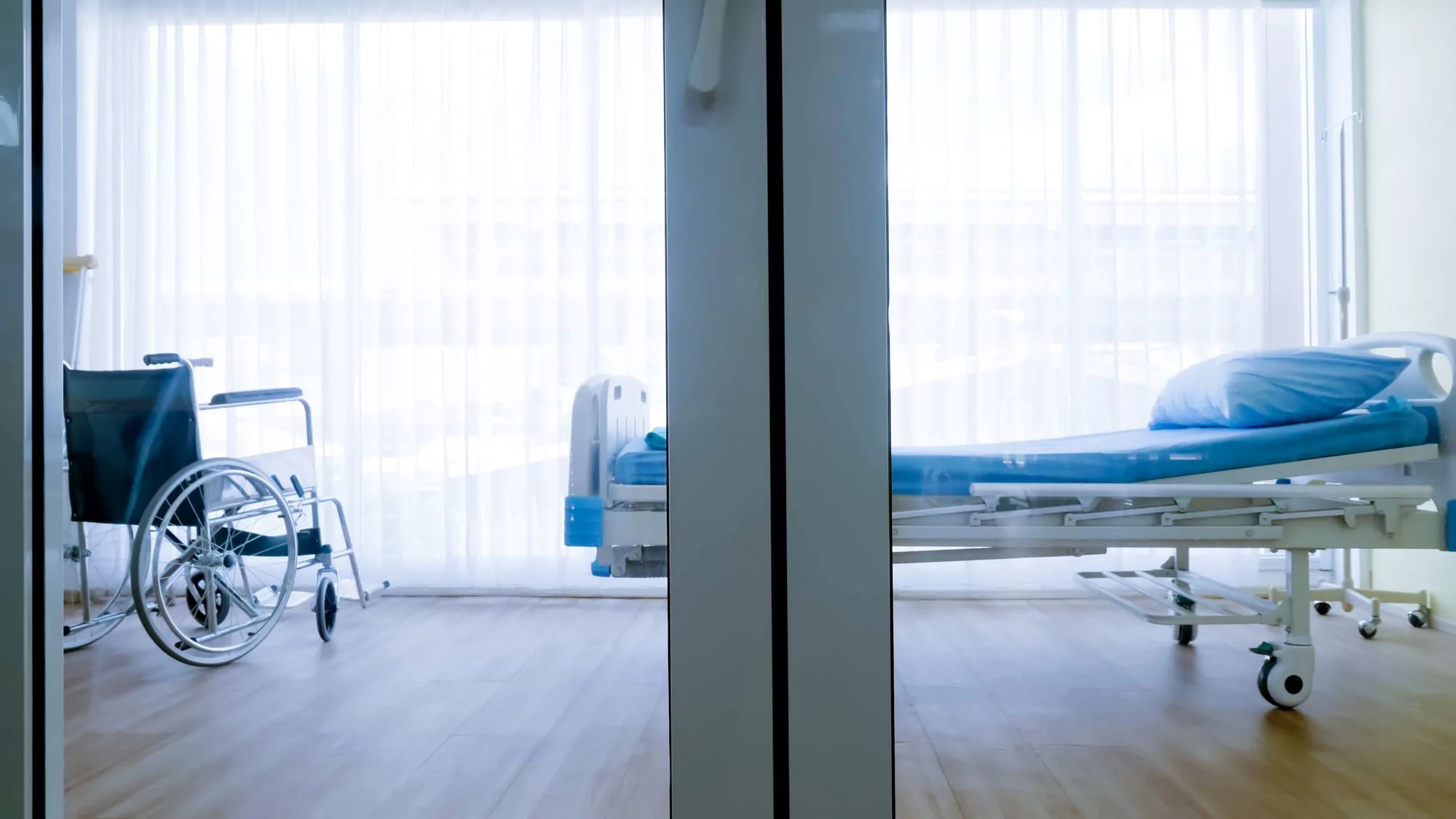 Empty hospital room with wheelchair behind glass door