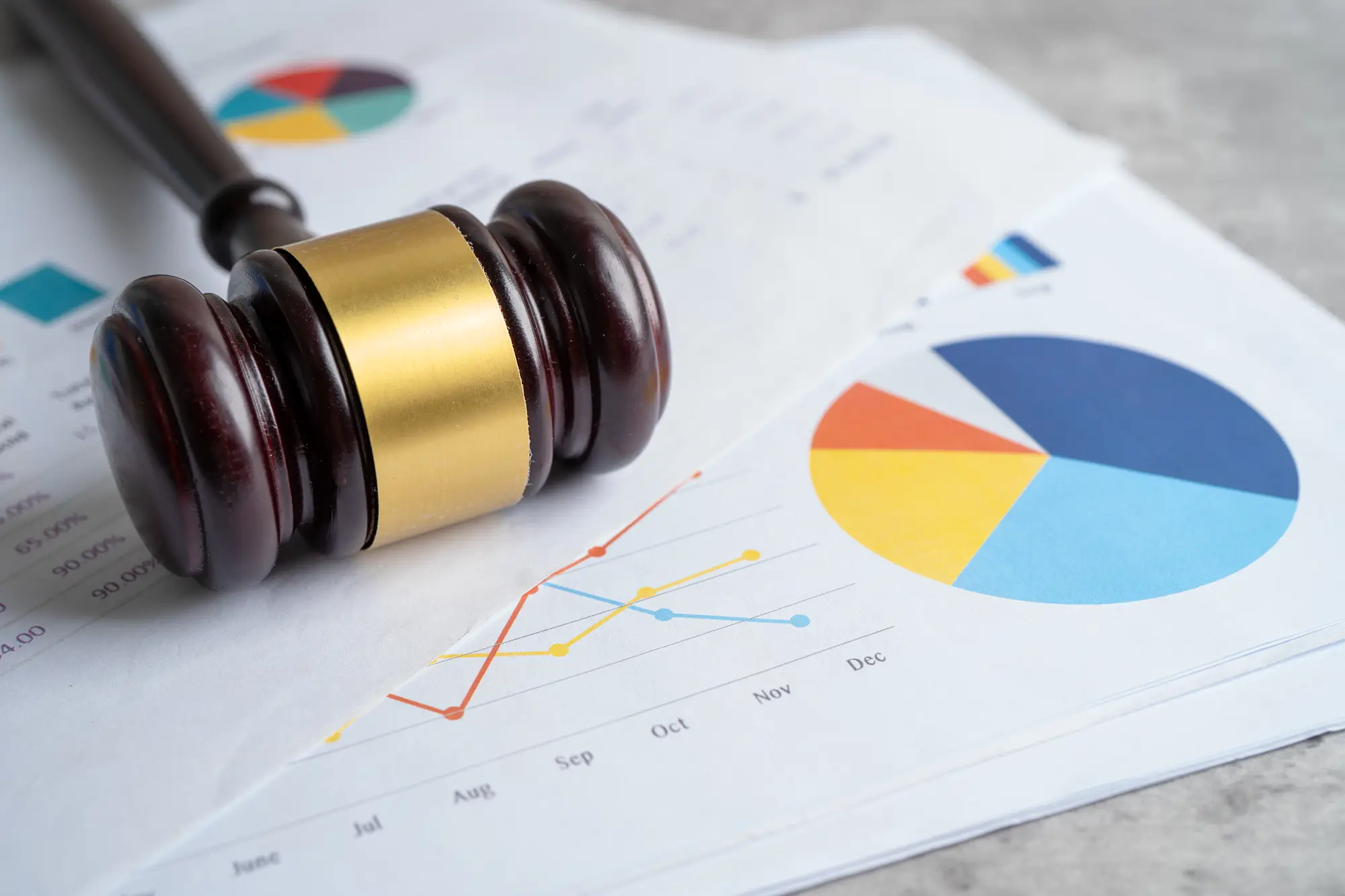 Wooden judge's gavel resting on printed charts and graphs, symbolizing legal action, compliance, audits, or regulatory enforcement.