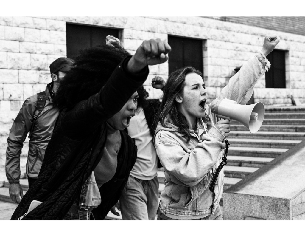 Medicaid advocacy protest with diverse activists raising fists, as a woman shouts into a megaphone.