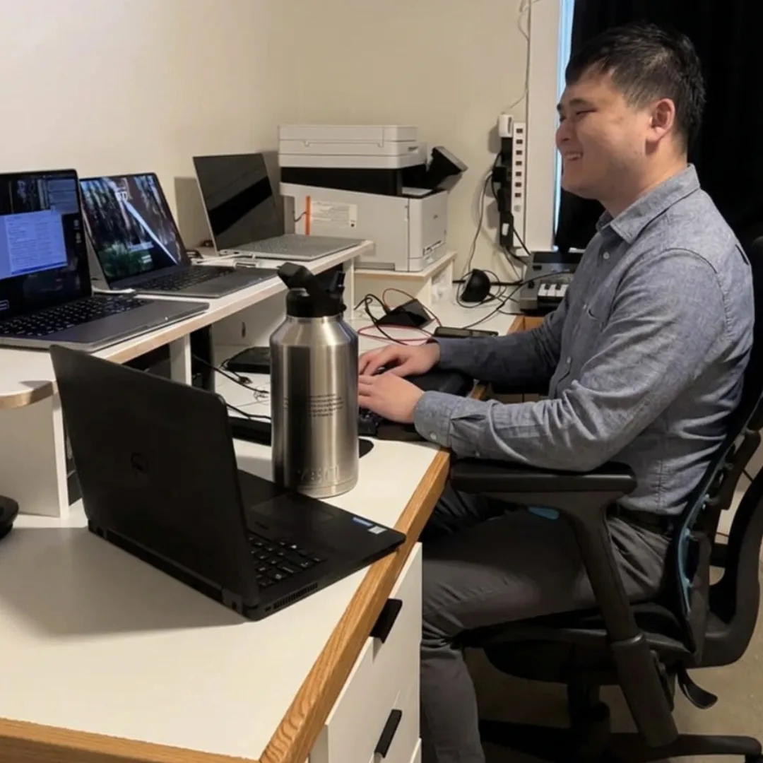 A blind man working at a desk with multiple laptops and a keyboard.