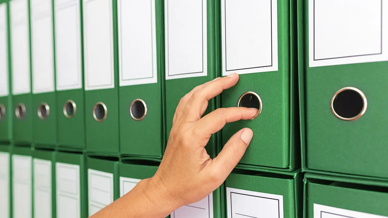 Hand reaching for green binders in a filing cabinet, representing archived documents stored in organizational records