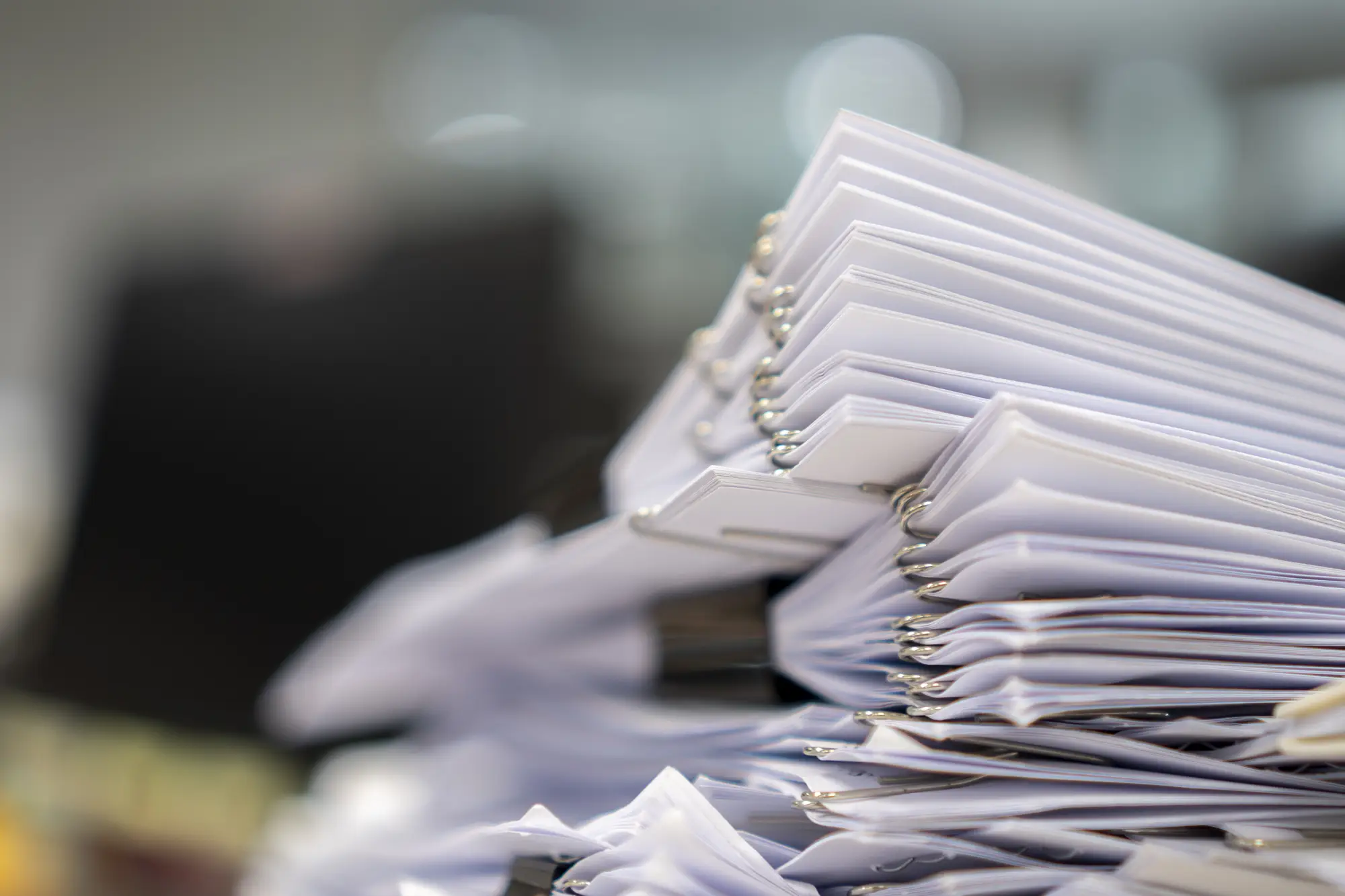 A stack of paper documents, with silver paperclips, blurry background