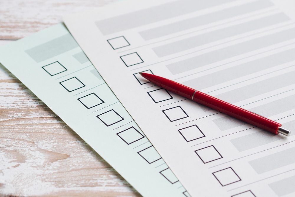 Two paper forms with empty checkboxes and a red pen resting on top