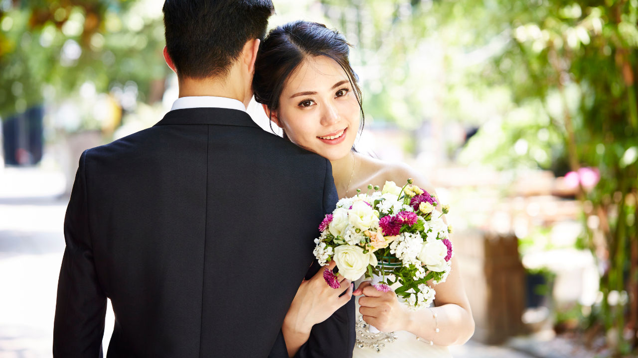 Bride holding bouquet smiles at camera while embracing groom in suit