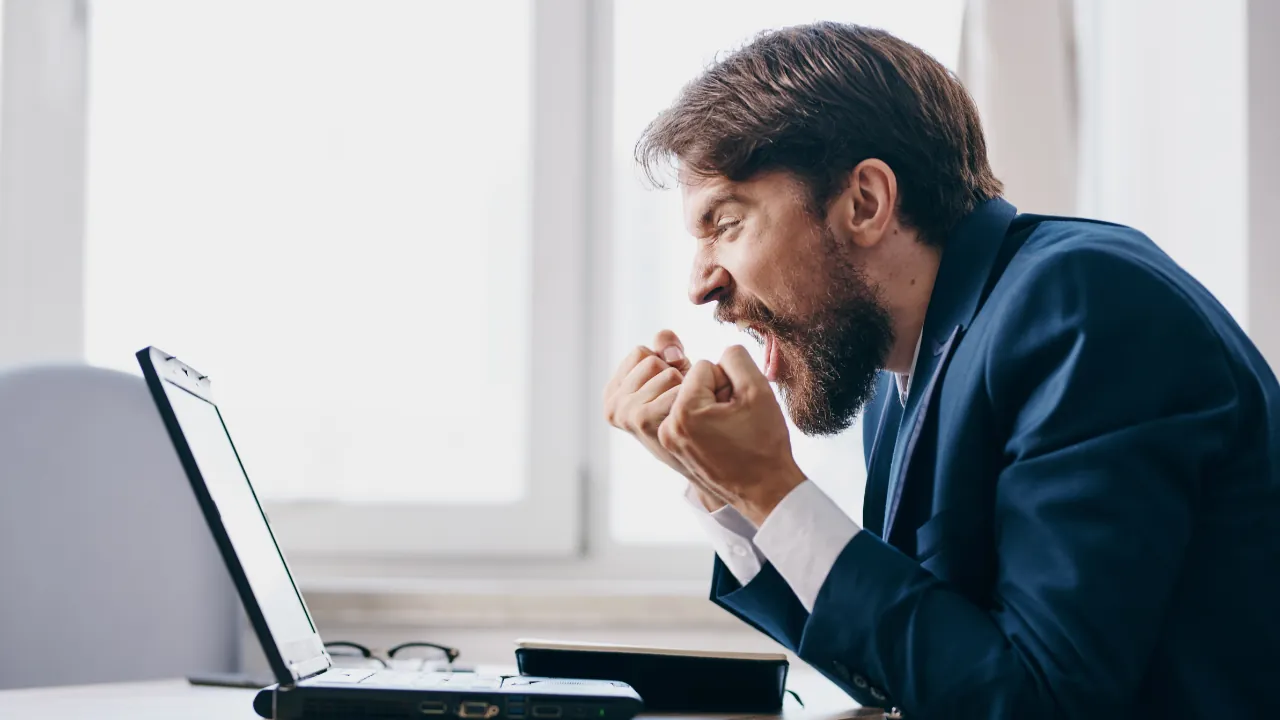Frustrated man in suit with clasped hands looking at laptop screen