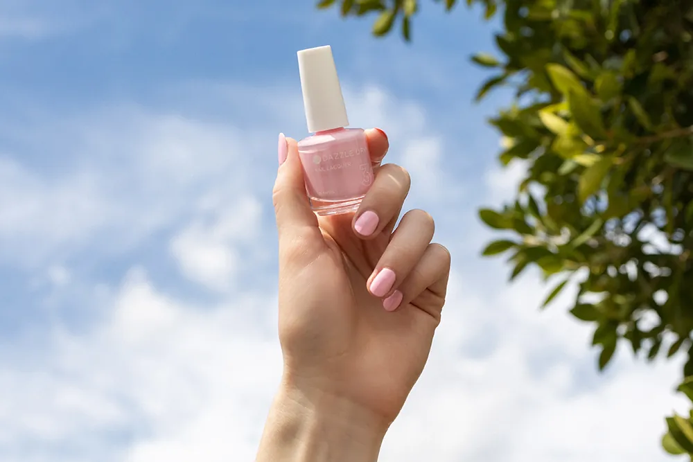 Hand holding pink nail polish bottle against blue sky background
