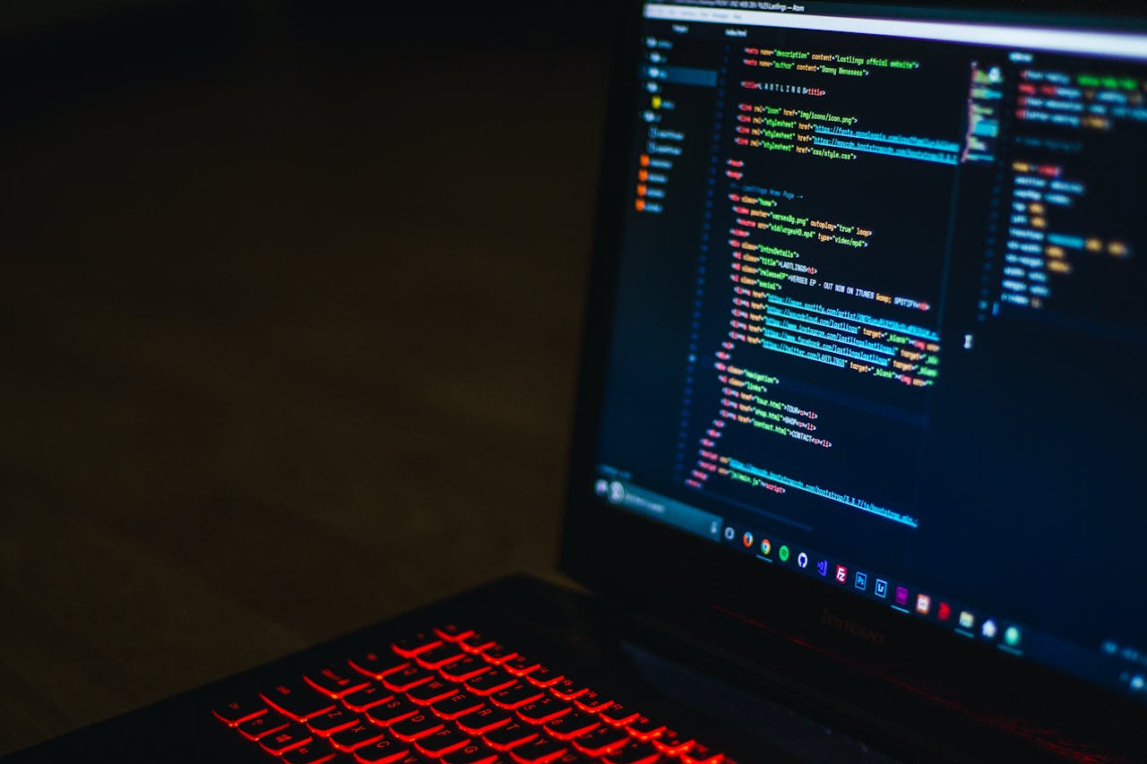 Laptop displaying colorful HTML code in a code editor with red backlit keyboard
