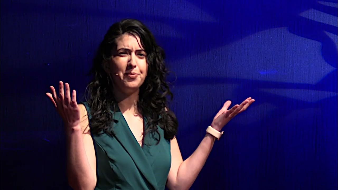 Woman with long dark hair speaking on stage against blue backdrop