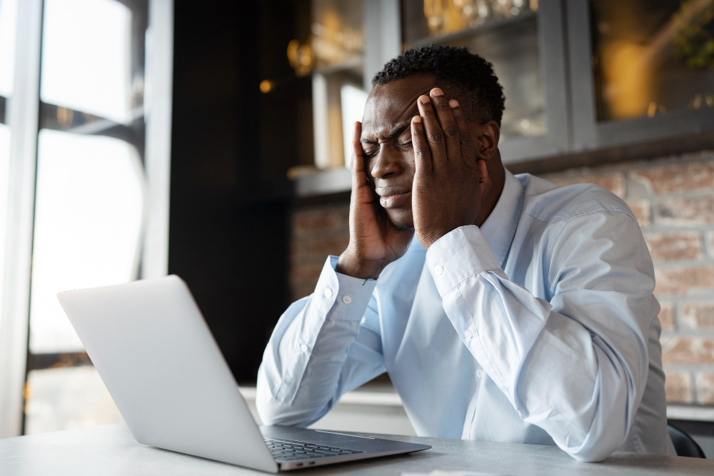 Man with hands on temples looking stressed while working at laptop