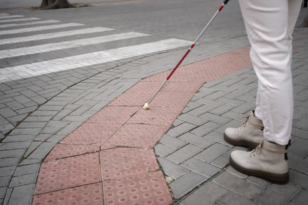 Person with white cane using tactile paving on sidewalk near crosswalk
