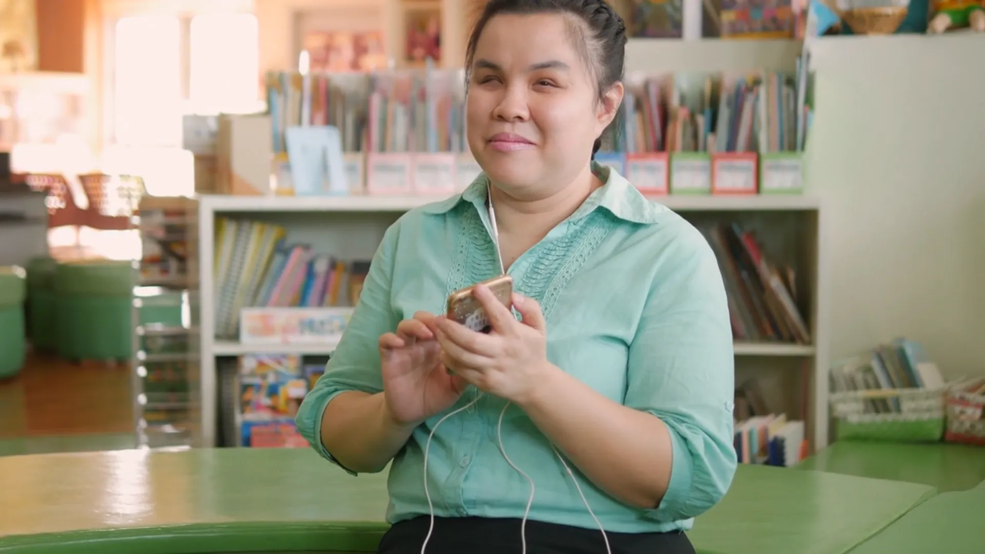 Woman wearing earbuds holds beverage in library or resource center