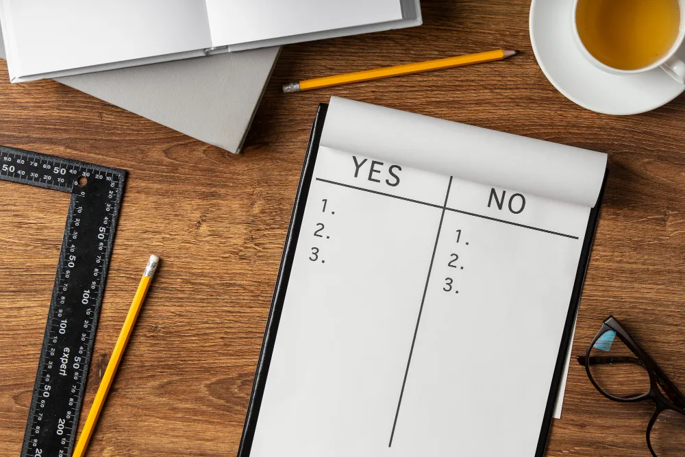 Notepad with YES and NO columns listing pros and cons, surrounded by office supplies